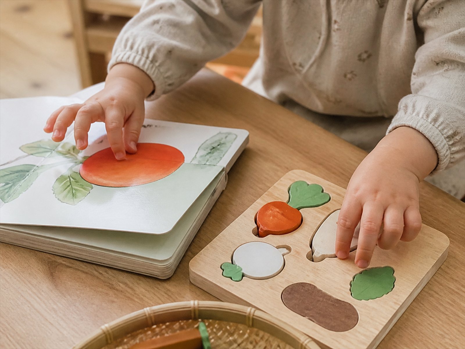 木のテーブルの上の絵本と木製パズルに伸びる子どもの手元