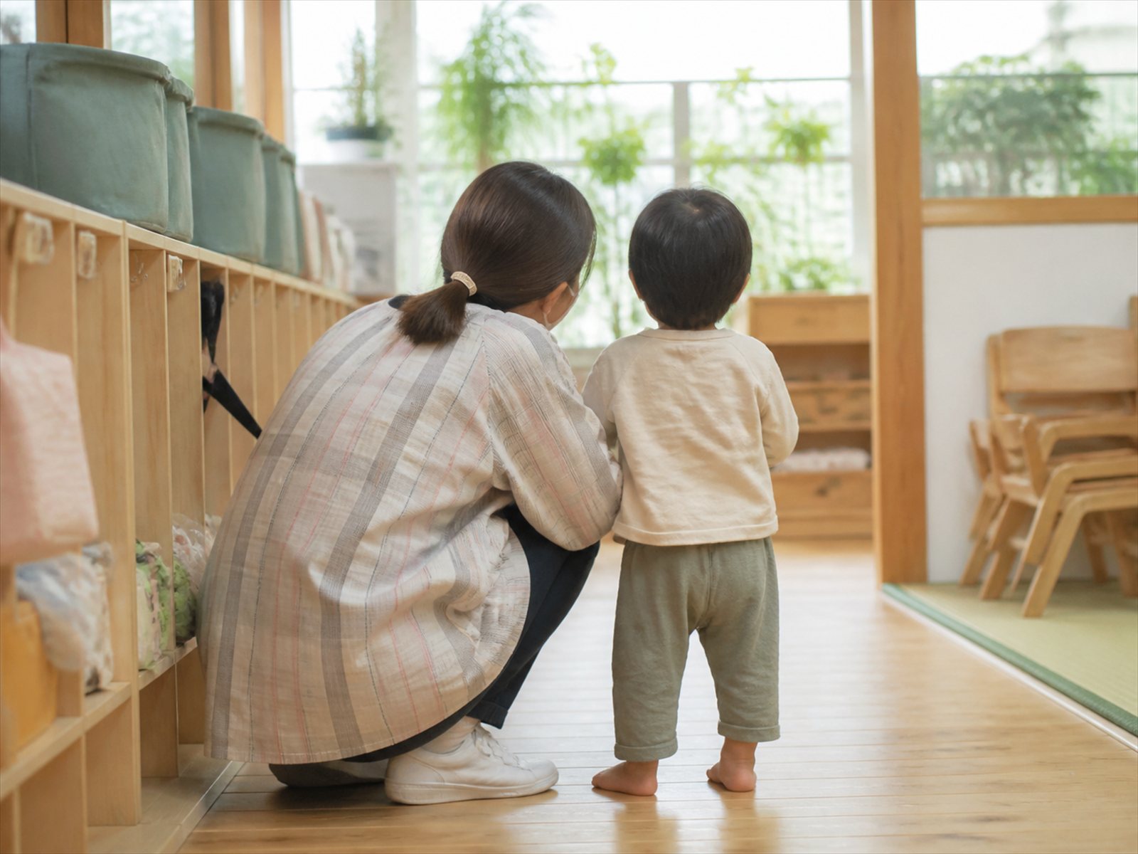 子どもと同じ目線にしゃがんで寄り添う保育士の後ろ姿